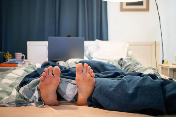 男でベッドでラップトップフォーカス上の足 — ストック写真