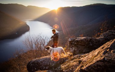 İnsan ve köpeği gün batımında muhteşem sonbahar manzarasının tadını çıkarıyorlar.