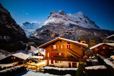 Kış gecesi Grindelwald karlı dağı, yıldızlar ve ahşap ev