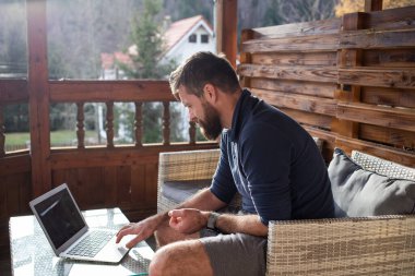 Ahşap kulübede dizüstü bilgisayarda çalışan bir adam.