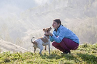 Baharda güzel dağ manzarasında köpeğiyle oynayan bir kadın.