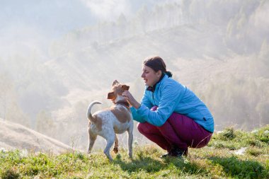 Baharda güzel dağ manzarasında köpeğiyle oynayan bir kadın.