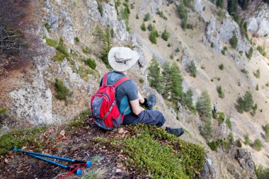 Erkek yürüyüşçü bir dağın tepesinde oturmuş manzaraya hayran.