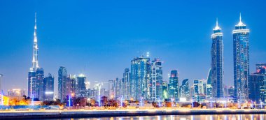 Dubai şehir merkezindeki gökdelenler üzerinde renkli günbatımı bayrağı ve Dubai su kanalından izlenen yeni inşa edilen Hoşgörü köprüsü