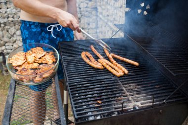 Arka bahçede barbekü yapıyor.