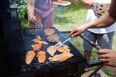 Arka bahçede barbekü yapıyor.