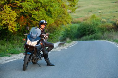 Motosikletli bir sürücü manzaranın tadını çıkarmak için ara veriyor. Motosikletli bir yaz gezisi.