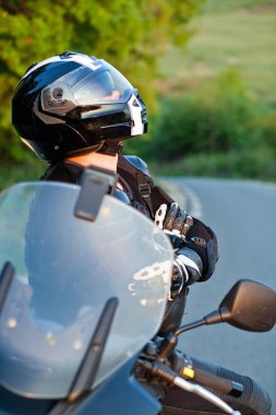 Motosikletli bir sürücü manzaranın tadını çıkarmak için ara veriyor. Motosikletli bir yaz gezisi.