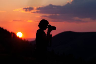 Gün batımının arka planında kamera olan bir adamın silueti.