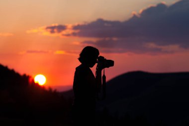 Gün batımının arka planında kamera olan bir adamın silueti.