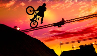 Gün batımında bisikletle atlayan bir adamın silueti.