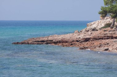 Bir uçurumun güneşli sahilinde mavi kumlu bir deniz suyunun dikey görüntüsü.