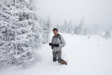 Kış ormanında yürüyen kameralı bir adam.