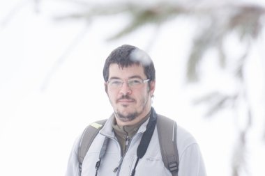 Kış ormanında yürüyen kameralı bir adam.