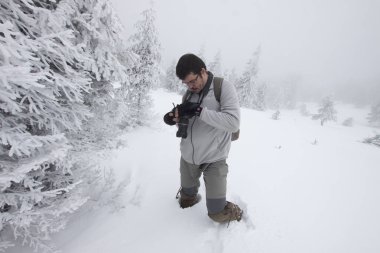 Kış ormanında yürüyen kameralı bir adam.