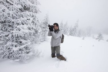 Kış ormanında yürüyen kameralı bir adam.