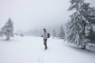 Kış ormanında yürüyen kameralı bir adam.