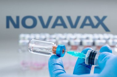 CLUJ-NAPOCA -ROMANIA - 9 Mart 2021: Novavax Aşısı Covid-19 konsepti. Şırınga iğnesi ve aşı. Arka planda Novavax şirketinin logosu bulanıklaşmış..