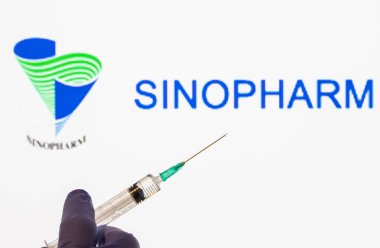CLUJ-NAPOCA -ROMANIA - 9 Mart 2021: Sinopharm aşısı Covid-19 konsepti. Şırınga iğnesi ve aşı, arka planda bulanık Sinopharm şirketi logosu..