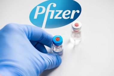 CLUJ-NAPOCA -ROMANIA - 9 Mart 2021: Pfizer aşısı Covid-19 konsepti. Şırınga iğnesi ve aşı, arka planda bulanık Pfizer şirket logosu..