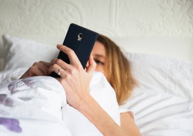 Yatakta akıllı telefon kullanan güzel bir kadın