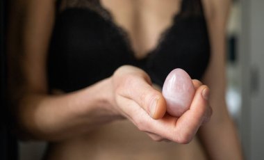 Elinde vajina yumurtası tutan bir kadın. Gül kuvars kristal yeşim yumurta. 