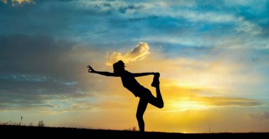 Gün batımında denge pozisyonunda olan bir kadın dışarıda yoga yapıyor.