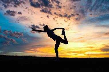 Gün batımında denge pozisyonunda olan bir kadın dışarıda yoga yapıyor.