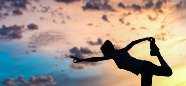 Gün batımında denge pozisyonunda olan bir kadın dışarıda yoga yapıyor.