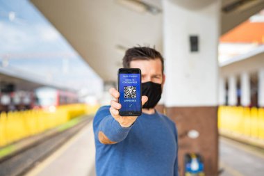 Coronavirus veya Covid-19 için sağlık aşısı pasaportu. Tren istasyonunda Uluslararası Seyahat Sertifikalı Seyahat İçin Bağışıklık Statüsü Aşısıyla Gezgin Cep Telefonu Kullanıyor