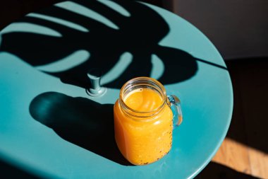 Yaz ışığında taze portakal suyu ve canavar ya da ayrık yapraklı filodendron yaprakları