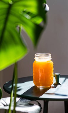 Yaz ışığında taze portakal suyu ve canavar ya da ayrık yapraklı filodendron yaprakları