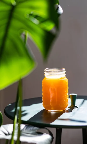 fresh orange juice in summer light and monstera or split-leaf philodendron leaves