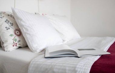 Temiz beyaz yastıklar ve yatakta açık bir kitap.
