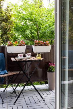 Yazın çiçekli ve kahve masalı küçük bir apartman terası.