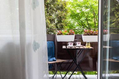 Yazın çiçekli ve kahve masalı küçük bir apartman terası.