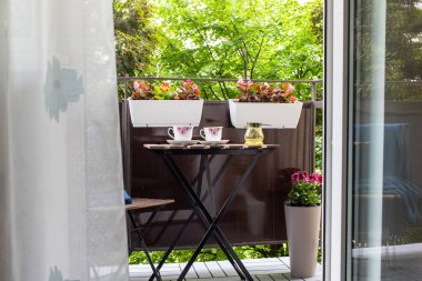 Yazın çiçekli ve kahve masalı küçük bir apartman terası.