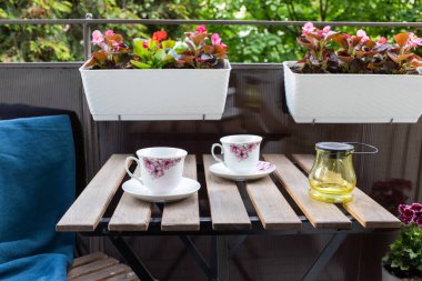 Yazın çiçekli ve kahve masalı küçük bir apartman terası.