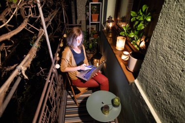 Yaz gecesi terasta dizüstü bilgisayarda çalışan bir kadın.