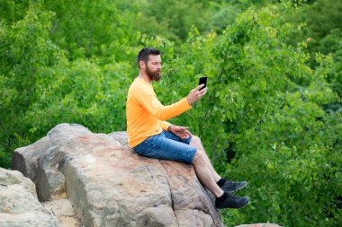 Yeşil yaz manzaralı bir kayanın üzerinde oturan yakışıklı adam.