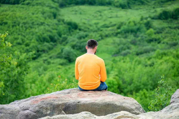 一个英俊的男人坐在岩石上 在绿色的夏季风景中 — 图库照片