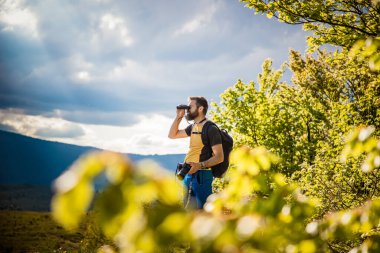Yakışıklı bir adam dürbünle doğada ağır ağır yürüyor.