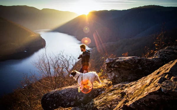 夕暮れ時には湖の景色を眺めながら岩の上に座っている男と犬 — ストック写真