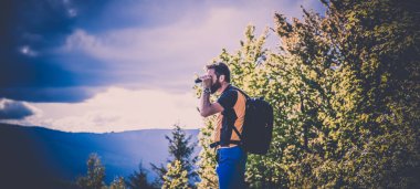 Yakışıklı bir adam dürbünle doğada ağır ağır yürüyor.