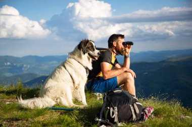 Yakışıklı adam ve beyaz köpek, dürbünle doğada ağır ağır ilerliyorlar.