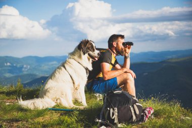 Yakışıklı adam ve beyaz köpek, dürbünle doğada ağır ağır ilerliyorlar.