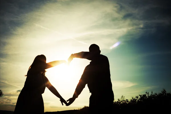 Silhouette di coppia amorevole che si tiene per mano a forma di cuore sopra o — Foto Stock