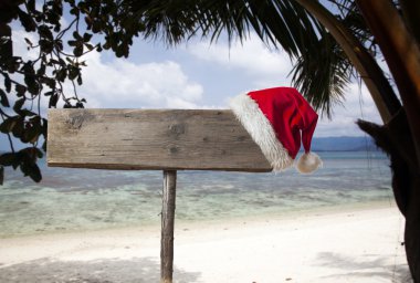 Tropik sahilde Noel şapka ile ahşap tabela 