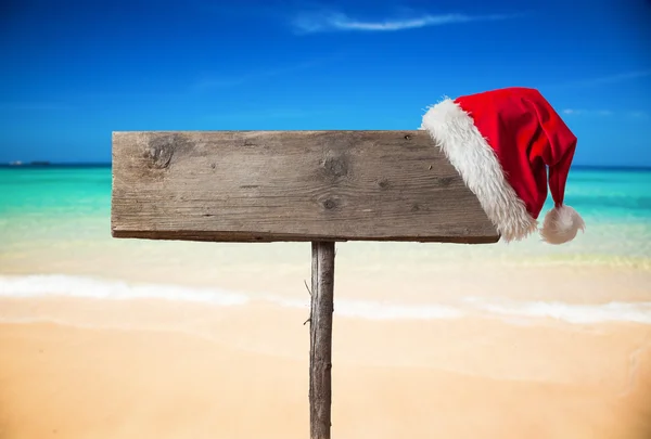 Placa de madeira com chapéu de Natal na praia tropical — Fotografia de Stock