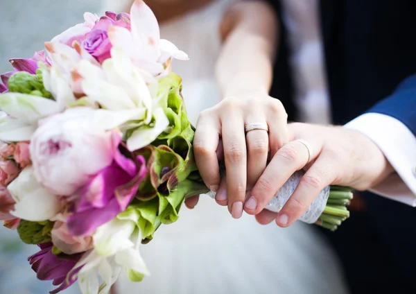 Mãos e anéis no buquê de casamento — Fotografia de Stock